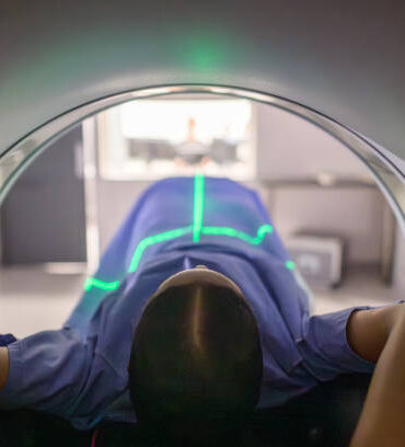 A patient positioned inside a modern CT scanner, illuminated by alignment lasers, undergoing a diagnostic scan. The setting is clinical, emphasizing precision, health care, and medical technology. This image portrays the importance of advanced medical tools in diagnosing and treating patients efficiently.